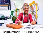 Small photo of tanzanian woman with snake print turban over hear working in dressmaking shop