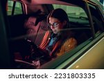 Businesswoman traveling with car on a business trip during night while sitting in a backseat and using a smartphone. Female using mobile phone to send email or messages. View trough car window.