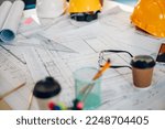 Blueprints with sketches of projects, laptop, helmet and some mechanical tools lying on a architect or engineer table in an office or construction site. Focus on a building plan. Copy space.