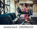 Small photo of Profile view of a fast female runner running on a treadmill in a gym. A healthy sportswoman is exercising on a treadmill in a gym. Sportswoman running on a treadmill.
