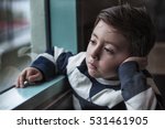 Small photo of Portrait of a somber little boy in blue and white stripped sweater staring outside through a window on a dark winter morning