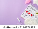 Small photo of Top view photo of red heart marks on the calendar pink menstrual cup period pads tampon and camomile bud on isolated pastel violet background with copyspace