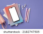 Back to school concept. Top view photo of smartphone over colorful diaries earbuds pens ruler clips and pink pencil-case on isolated purple background with blank space