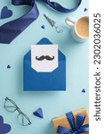 Small photo of Father's Day surprise idea. Top view vertical of open envelope, postcard with mustaches, coffee mug, tie, glasses, craft paper giftbox with bow, and other men's accessories on pastel blue background