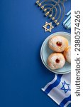 Small photo of Observe Hanukkah with tasteful table setup. Overhead vertical shot of traditional Jewish dish - sufganiyot on plate, Star of David, Israel flag, menorah on blue backdrop with blank area for your text