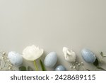 Small photo of Spring celebration theme in top view photo featuring slate greyish eggs, a bunny statuette, gypsophila, tulip, and eucalyptus arrayed on a soft grey canvas, with a void for text or advertising