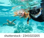 Father and daughter are snorkeling next to a beautiful sea turtle