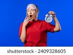 Small photo of Woken up by alarm clock sleepy young woman holding it in hand. Blue background. Early 8 o'clock in morning. Lazy guy didn't get enough sleep, concept of passing time. High quality 4k