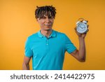 Small photo of Woken up by alarm clock sleepy african man holding it in hand. Yellow background. 10 o'clock in morning. Lazy guy didn't get enough sleep, concept of passing time. High quality