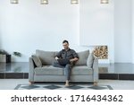 Man working on a laptop with crossed legs. Large bright living room. Working from home