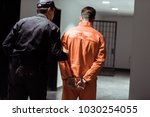 rear view of prison officer leading prisoner in handcuffs in corridor