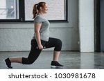 Plus size woman performing lunges with dumbbell in gym