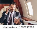 handsome businessman in suit listening music and using smartphone in private plane 