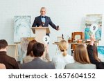 selective focus of auctioneer holding gavel and microphone and looking at buyers during auction