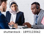 arabian and african american business people in headsets near digital translators and interpreter on blurred foreground