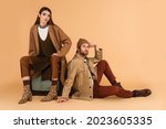 trendy woman sitting on vintage tv set near stylish man on floor on beige background
