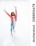 Small photo of high angle view of cheerful young woman in ear muffs and scarf showing peace sign while skating on ice rink
