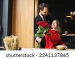 bearded man in suit holding bouquet of red roses near smiling girlfriend on valentines day