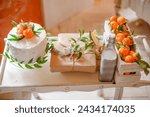 White cake decorated with fresh tangerines, gift wrapped in kraft paper and milk on table at decorated party to gender party