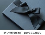 Black gift box on a dark contrasted background, decorated with a textured bow and feathers, creating a romantic atmosphere. Typically used for birthday, anniversary presents, gift cards, post cards.