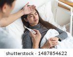 Sick day at home in winter season. Young asian woman lying on the bed have a fever and her husband checking thermometer and measure body temperature.