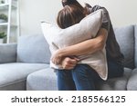 Small photo of Unhappy anxiety young Asian woman covering her face with pillow on the cough in the living room at home.