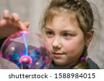 Portrait of a little girl playing with a plasma ball. The child touches the surface of the lamp, causing lightning. Selective focus.
