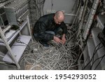 Small photo of A technician sits on wires in a ransacked server room. The man reconnects at the abandoned datacenter. An engineer repairs equipment of an old TV station