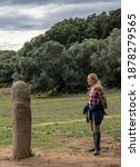 Small photo of Young blonde woman meets a phallic statues in Megalithic site in Corsica, France