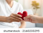 Small photo of Young and senior woman holding each other hands and red yarn heart shape togetherness concept. Elderly care and protection with love from grandchild.