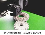 Small photo of print head, bright green print bed and white helical gears with visible infill and layer. opblique view on process of 3D-printing. copy space for text. selective focus. additive manufacturing concept