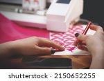 Small photo of woman with painted nails weeds freshly cut peace dove stickers in pink color from carrier film. wooden worktop with plotting machine in background and mobile phone in forground. selective focus