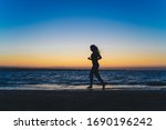 Silhouette of beautiful long hair girl standing on sea beach and looking on sunset. Running and jumping on sea.