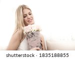 The young blonde holds a bouquet of flowers in her hands in a decorative box she received from a man she loves. She laughs and is very happy.