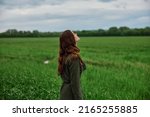 Small photo of a beautiful, red-haired girl in a raincoat stands in a field in the spring in rainy weather. High quality photo