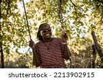 Happy smiling young Woman swinging in autumn sunny day among tree leaves in the park. African American female with eyeglasses on swing outdoor
