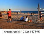 Small photo of Laguna Beach, CA, USA July 22, 2014 A young man jogs on the boardwalk while others partake in a game of beach volleyball on a summer day in Laguna Beach, California
