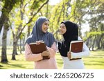Asian young Muslim woman wear hijab grey and black headscarf and hijab dress stand and holding a book in the park. Leisure after study and practices in Islam