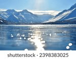 Small photo of A serene winter scene unfolds as a frozen lake sits peacefully beneath snow-capped mountains. The tranquil landscape is painted in shades of white and blue.