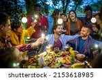 Large group of happy friends singing and having fun during dinner on balcony, mixed age range people celebrating holiday eating together, people hugging each other and using mobile phone lights