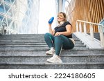 Plus size woman having a break during her workout, curvy young woman in sportswear in cardiovascular training sitting on steps and drinking water, fitness in the city lifestyle, copy space