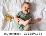 baby in a green cotton bodysuit is crying lying in bed with wooden educational toys. top view. products for children, early development, nursery kindergarten. space for text. High quality photo