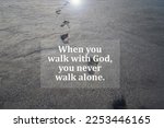 Spiritual inspirational quote - When you walk with God, you never walk alone. With footprints on beach black sand background. Believe in God concept.