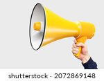 Hand with yellow loudspeaker. Man holds out loudspeaker. Place for text next to megaphone. Copy space on white background. Loud-hailer symbolizes ads and promotional calls. Agitation metaphor