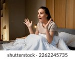 Small photo of A shocked woman who overslept with her mouth open from screaming. A young upset, tense lady is late. the surprised girl wakes up scared from a nightmare, on the bed in the bedroom in the morning