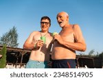 Small photo of Tow men on the beach drinking cold beverages from plastic cups. Summer manhood vacation, beer or cocktails bar at the pool. Retirement, mature son and father
