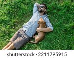 Top view of man and dog lying on green grass. Attractive European man is hugging his dog.