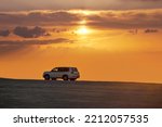 Small photo of Sealine, Qatar - October 07, 2022: Toyota Landcruiser 4WD driving through dunes at sunset time. dune bashing as part of a desert safari in Qatar