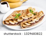 Crepes stuffed with chocolate spread and banana on white plate. Thin pancakes, blini. Sweet dessert.