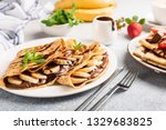 Chocolate hazelnut spread and banana filled crepes on plate. Tasty crepes or blini with sweet sauce and fruits. Closeup view